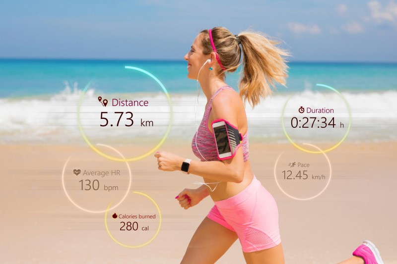 Frau joggt mit Fitnesstracker und Smartphone am Strand