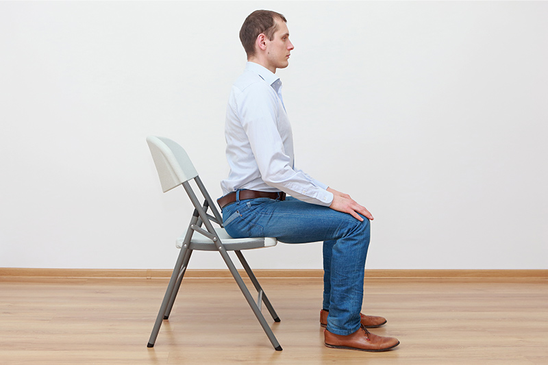 Mann sitzt in aufrechter Haltung auf einem Stuhl